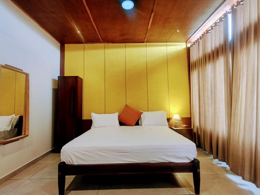 Cosy villa bedroom with yellow walls and lake-facing curtains at Kyna Backwaters