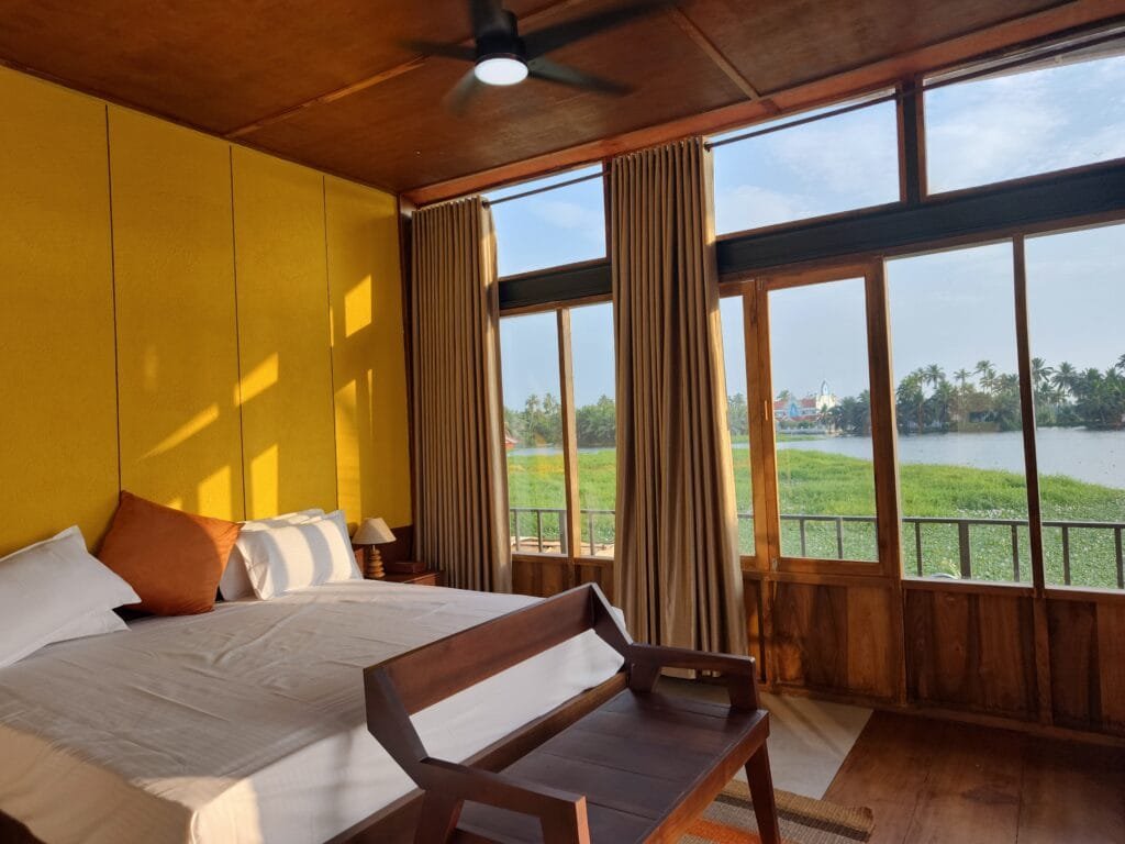 Villa bedroom with warm yellow walls and wooden ceiling at Kyna Backwaters, Kainakary