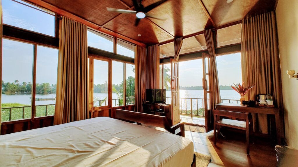 Bedroom with lake view windows and wooden ceiling at Kyna Backwaters, Alleppey