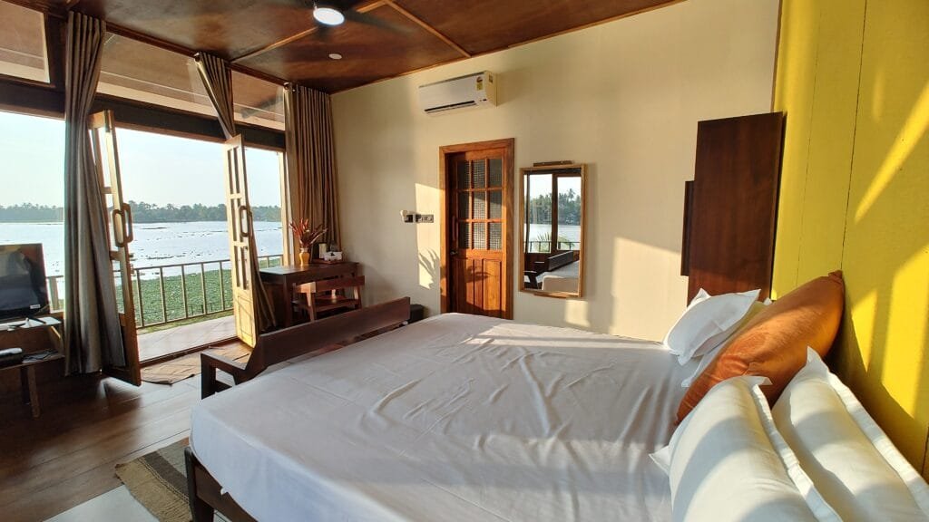 Bright bedroom with white linen and lake view windows at Kyna Backwaters, Alleppey